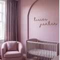 Wood baby name sign reading louise parker on a mauve nursery wall with an arch detail