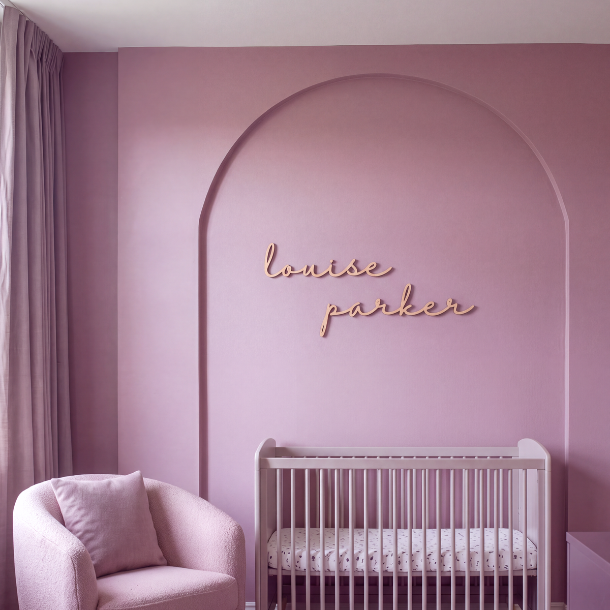 Cursive wood name sign above a crib in a pink nursery with an arched wall feature