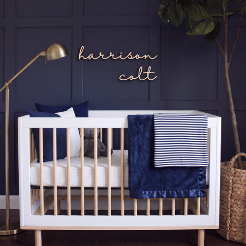 Cursive wood name sign reading harrison colt above a white crib in a navy nursery