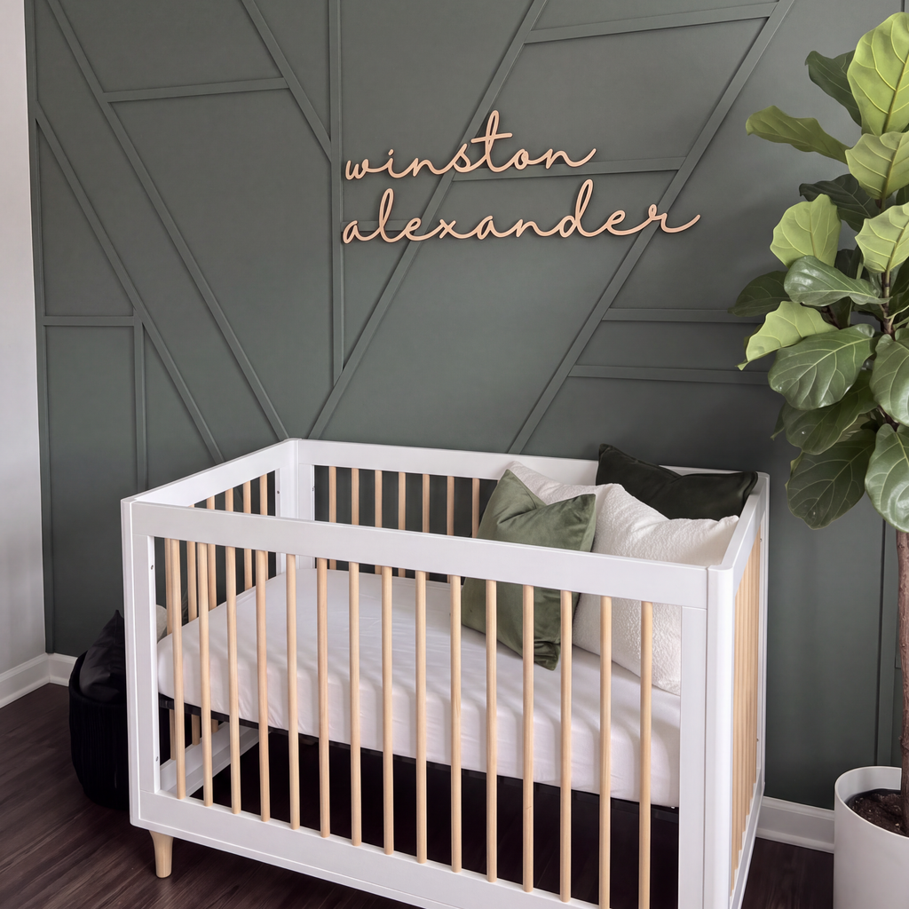Natural wood cursive name sign in a green nursery with a fiddle leaf fig and white crib