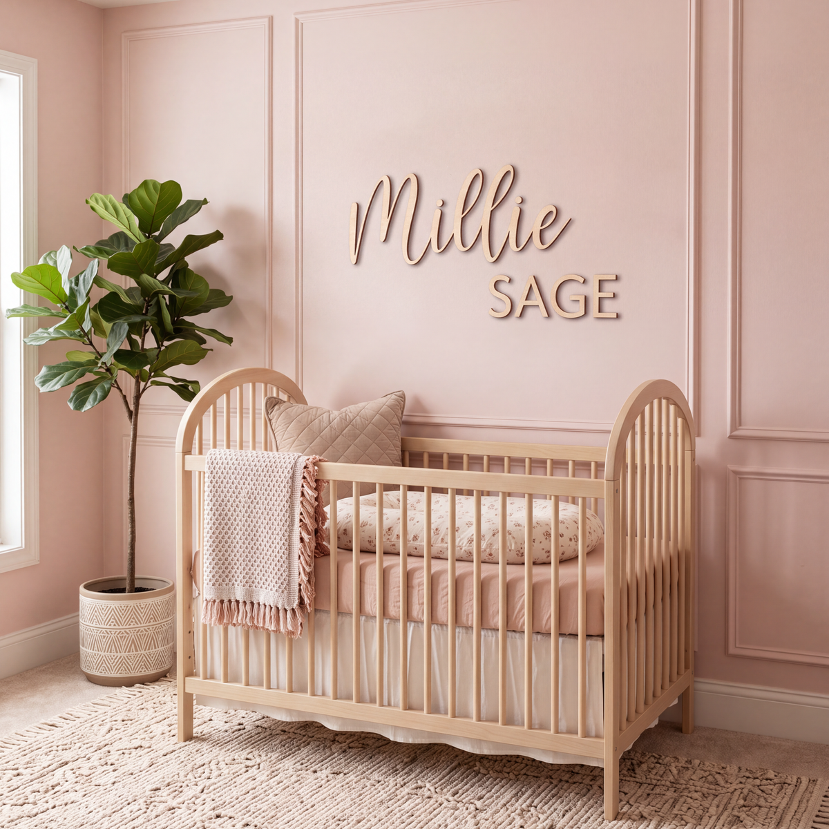 Cursive name sign in a blush nursery with a natural wood crib and fiddle leaf fig