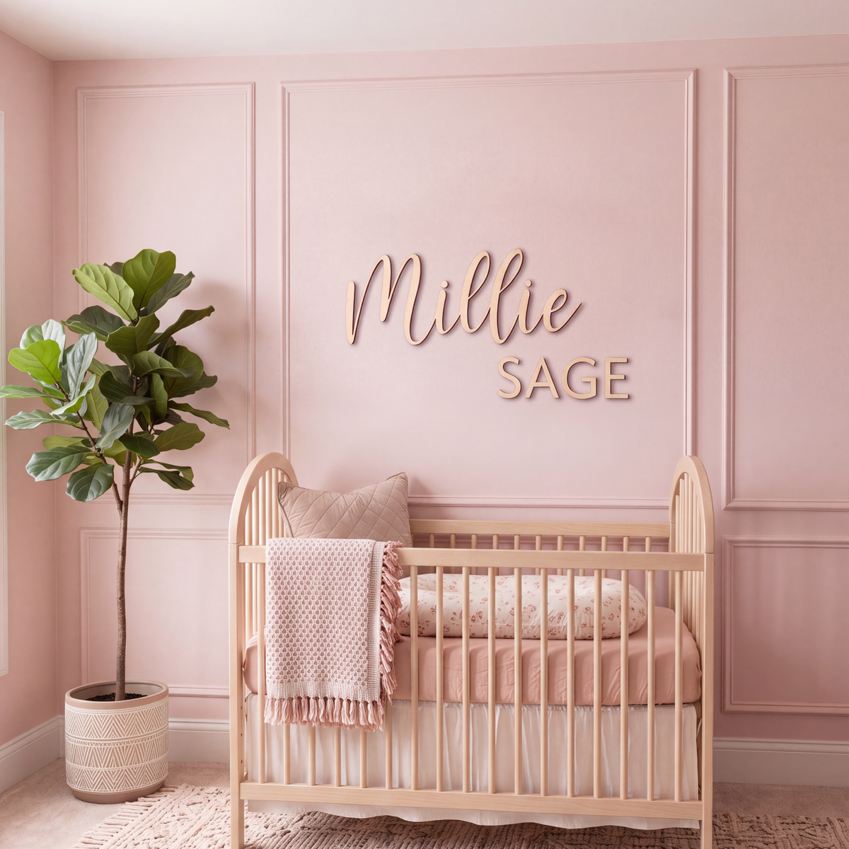 Wood nursery name sign reading Millie Sage on a blush panelled wall above a wooden crib