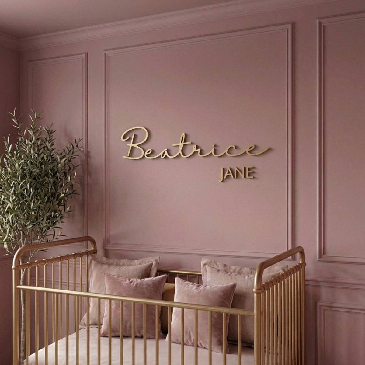 Gold cursive name sign above a gold crib in a pink panelled nursery