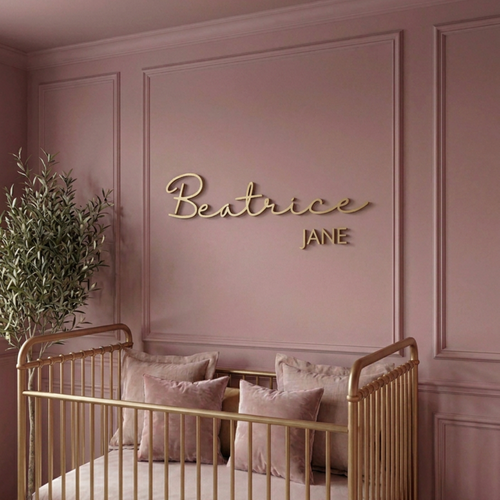 Gold cursive name sign above a gold crib in a pink panelled nursery