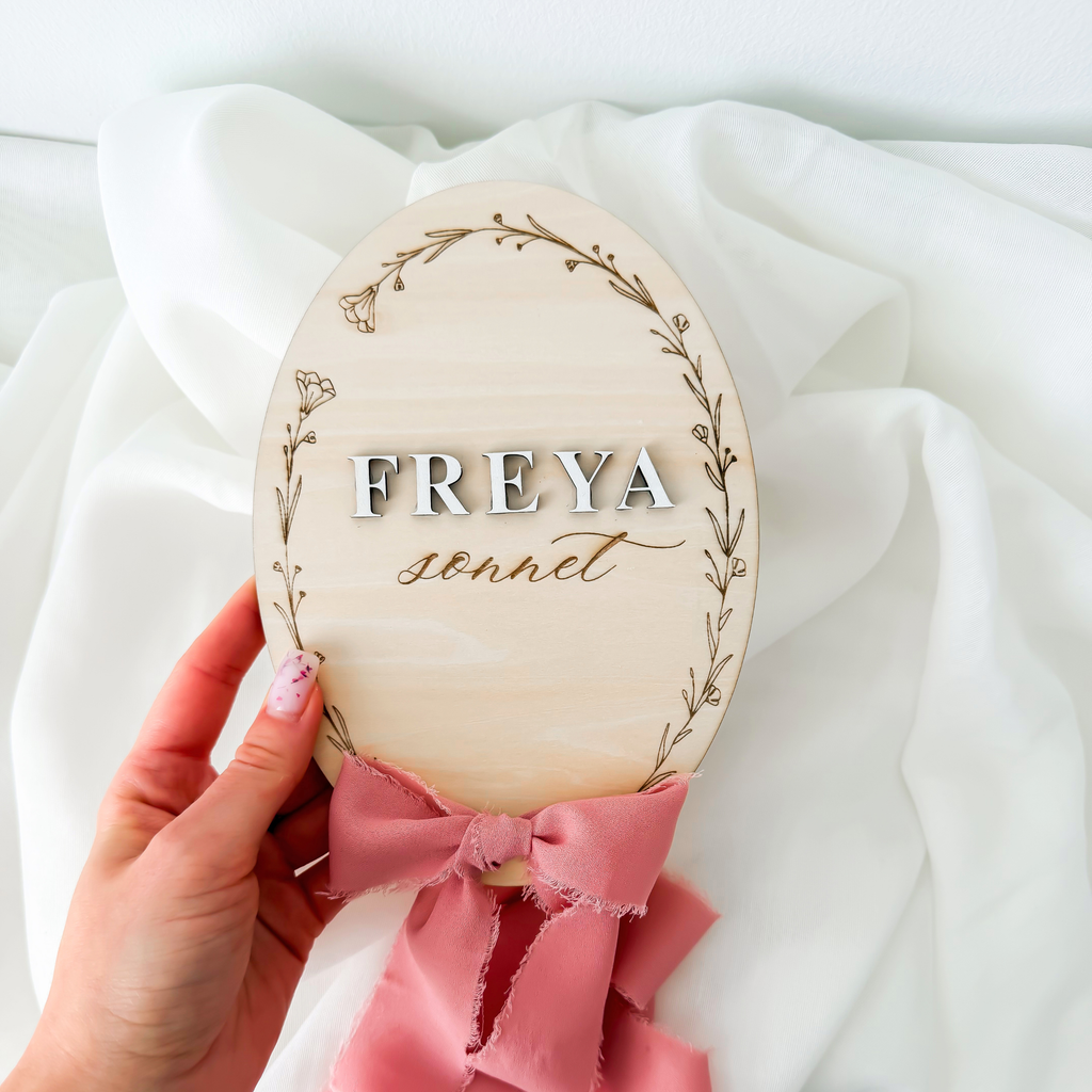 Hand holding the raised letter floral name sign with a dusty rose silk ribbon