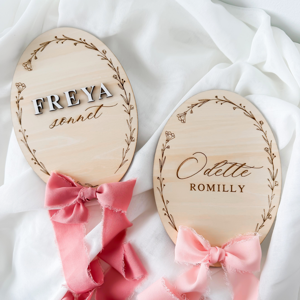 Two floral wreath name signs, one raised lettering and one engraved script, with rose ribbons