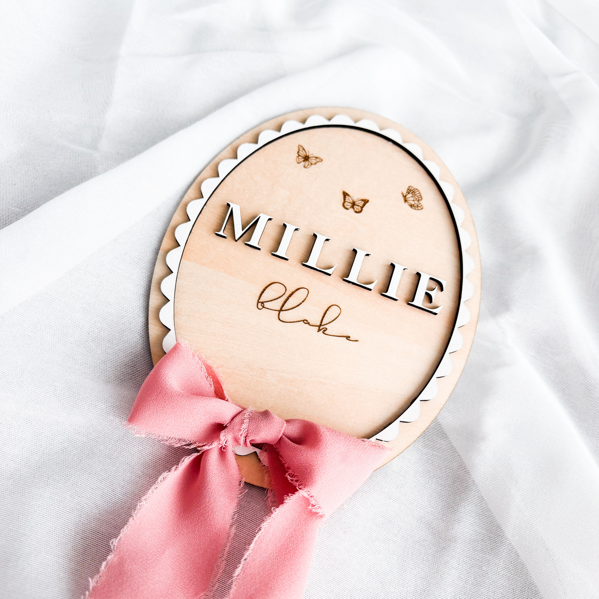 Butterfly baby name sign with a pink silk ribbon bow on white fabric