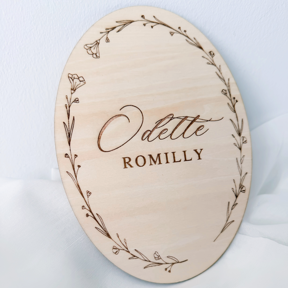 Angled view of the oval name sign showing the full engraved wildflower wreath border
